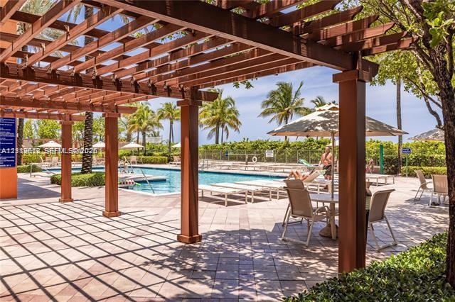 Outdoor space featuring a timber-frame pergola, stone paver terrace, swimming pool, and mature palm trees