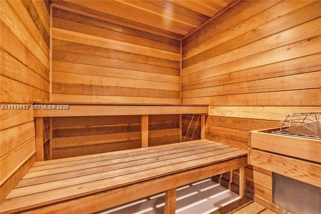 Sauna featuring natural wood tongue-and-groove paneling, tiered wood bench seating, and a built-in heating element
