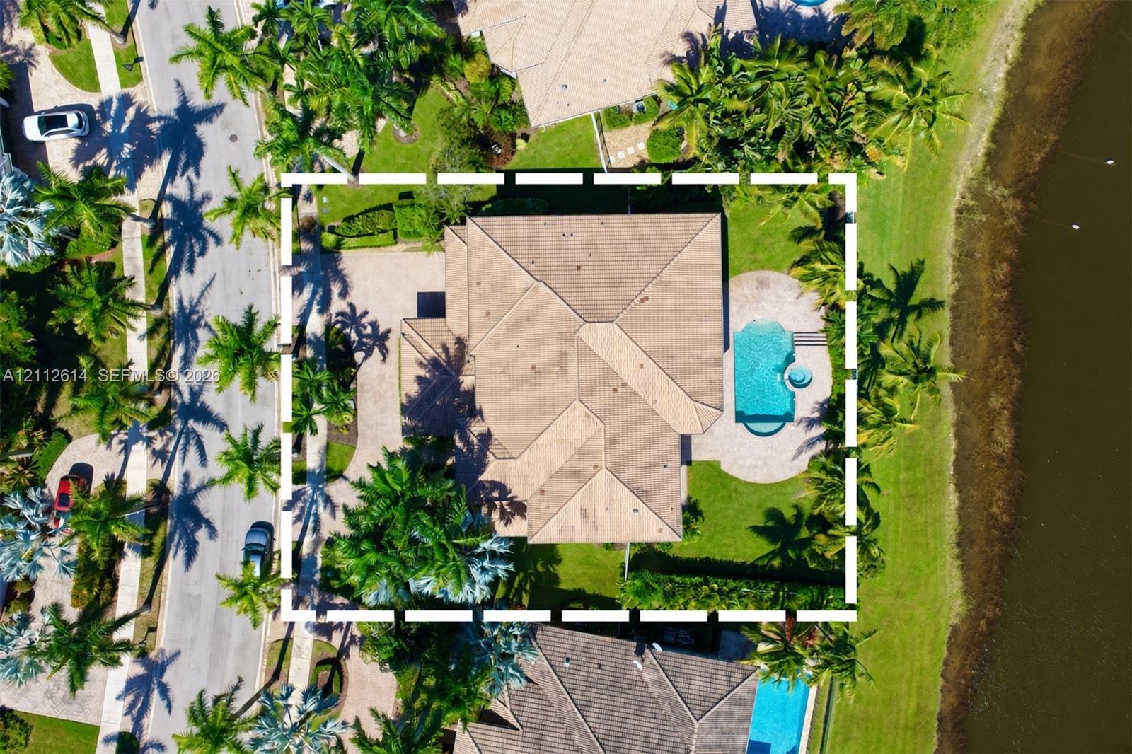 Aerial perspective of a property featuring a tile roof, an integrated swimming pool with a spa, paver hardscaping, and waterfront positioning