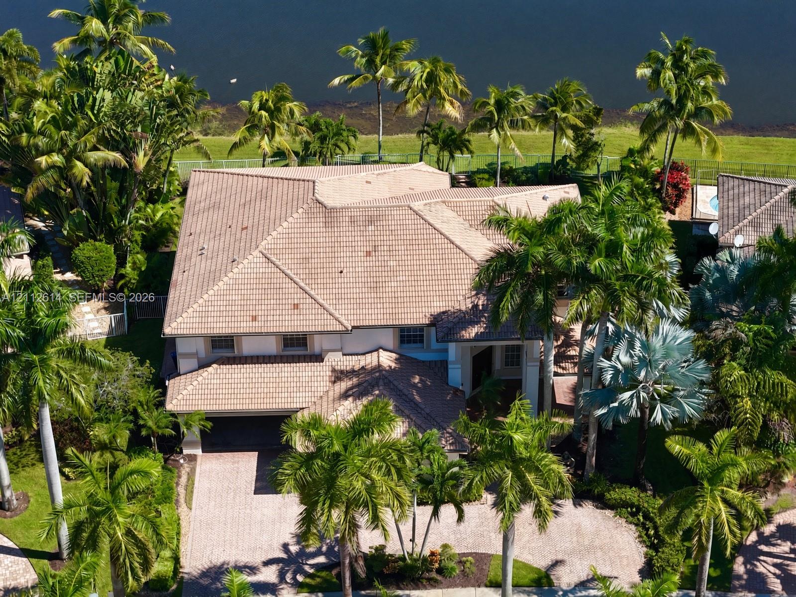 Multi-level residence featuring a tile roof, paved driveway, and mature landscaping on a waterfront lot Multi-level residence featuring a tile roof, paved driveway, and mature landscaping on a waterfront lot