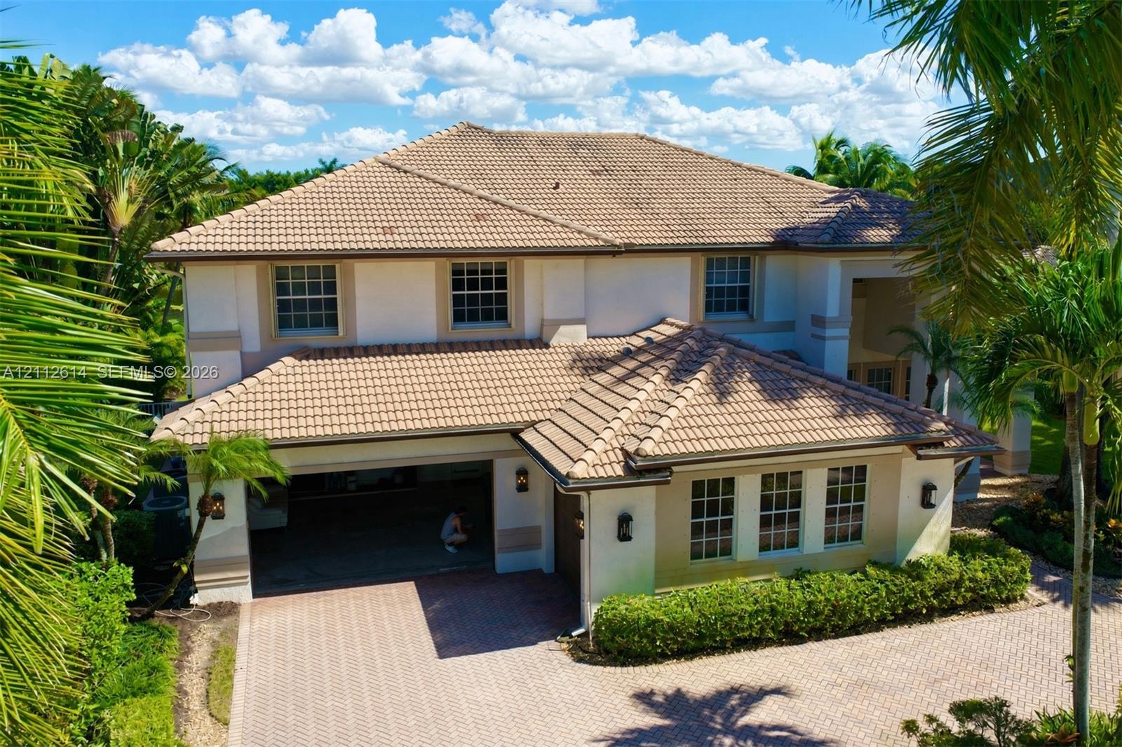 Two-story stucco exterior featuring a multi-hipped tile roof, paver driveway, multi-car garage, and grid-pattern window panes Two-story stucco exterior featuring a multi-hipped tile roof, paver driveway, multi-car garage, and grid-pattern window panes