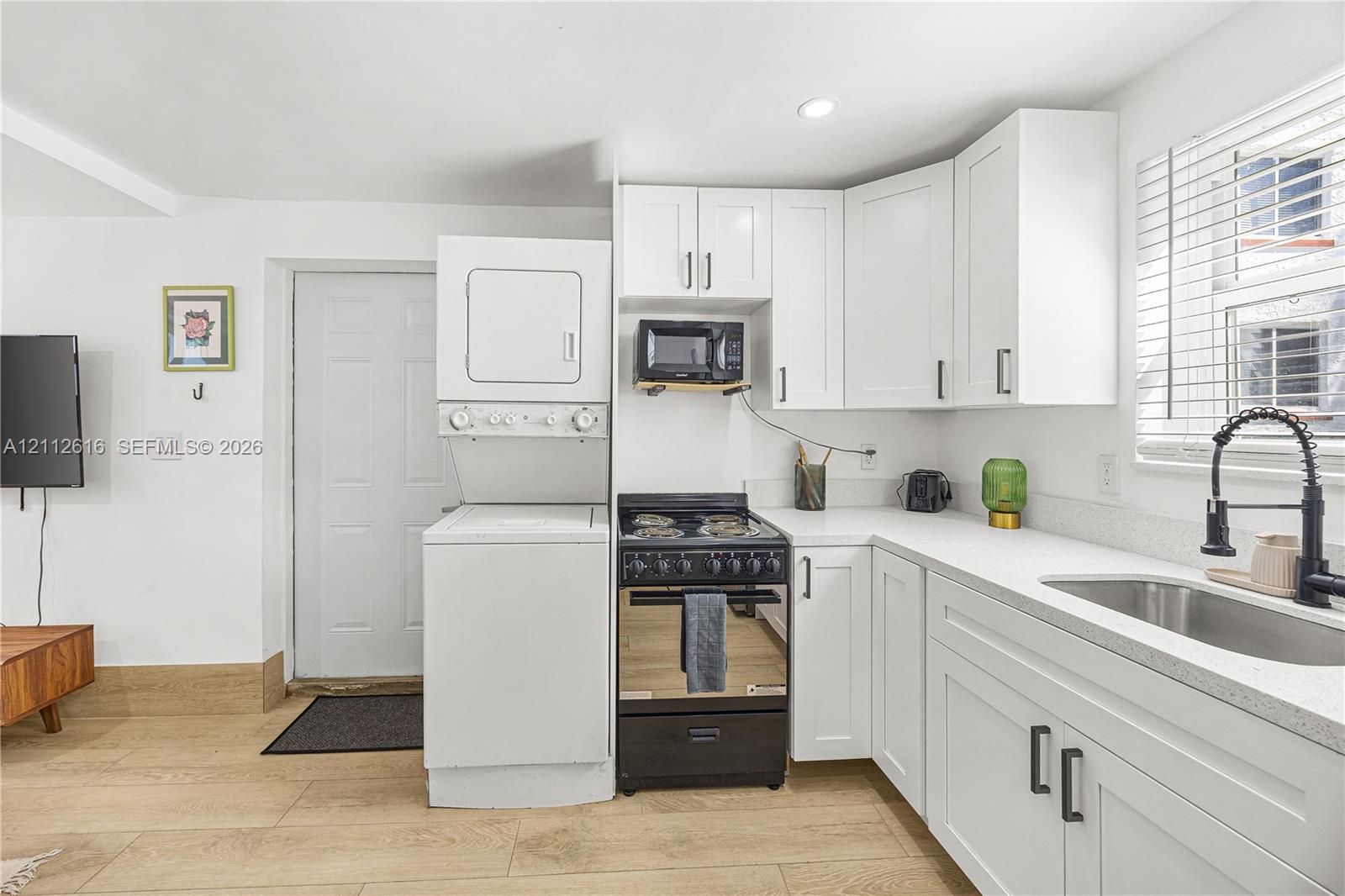 Kitchen featuring white cabinetry, solid-surface countertops, a stainless steel sink with a matte black faucet, a built-in laundry center, and wood-finish flooring