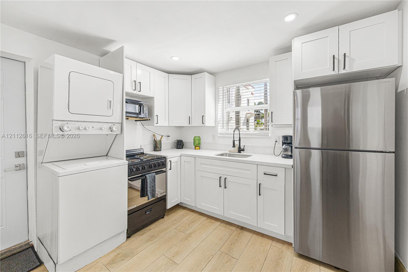 Kitchen featuring white Shaker-style cabinetry, stainless steel refrigerator, black gas range, wood-finish flooring, and recessed lighting
