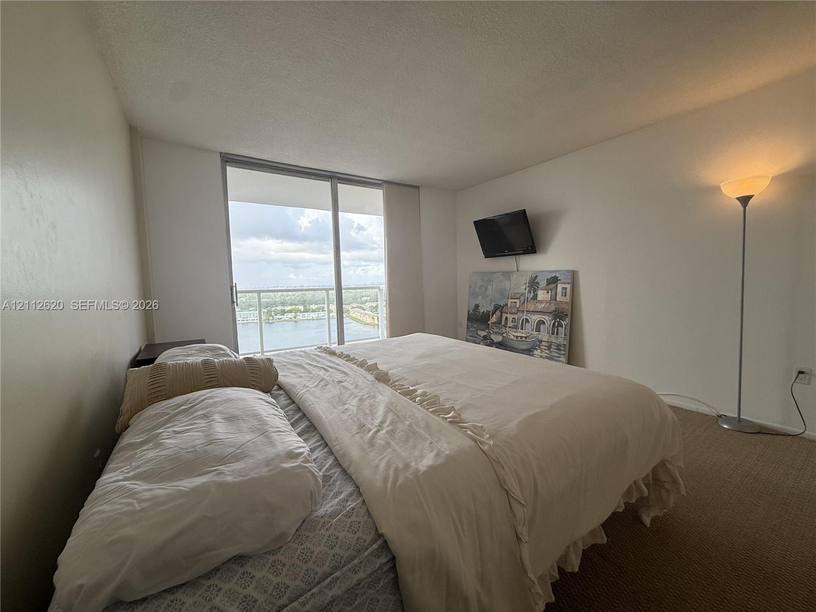 Floor-to-ceiling sliding glass door providing natural light and exterior water scenery, accompanied by a private balcony with a metal railing
