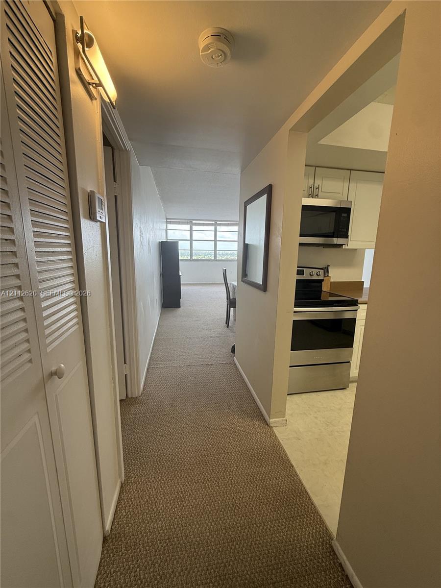 Hallway featuring louvered-door closet storage, neutral carpeting
