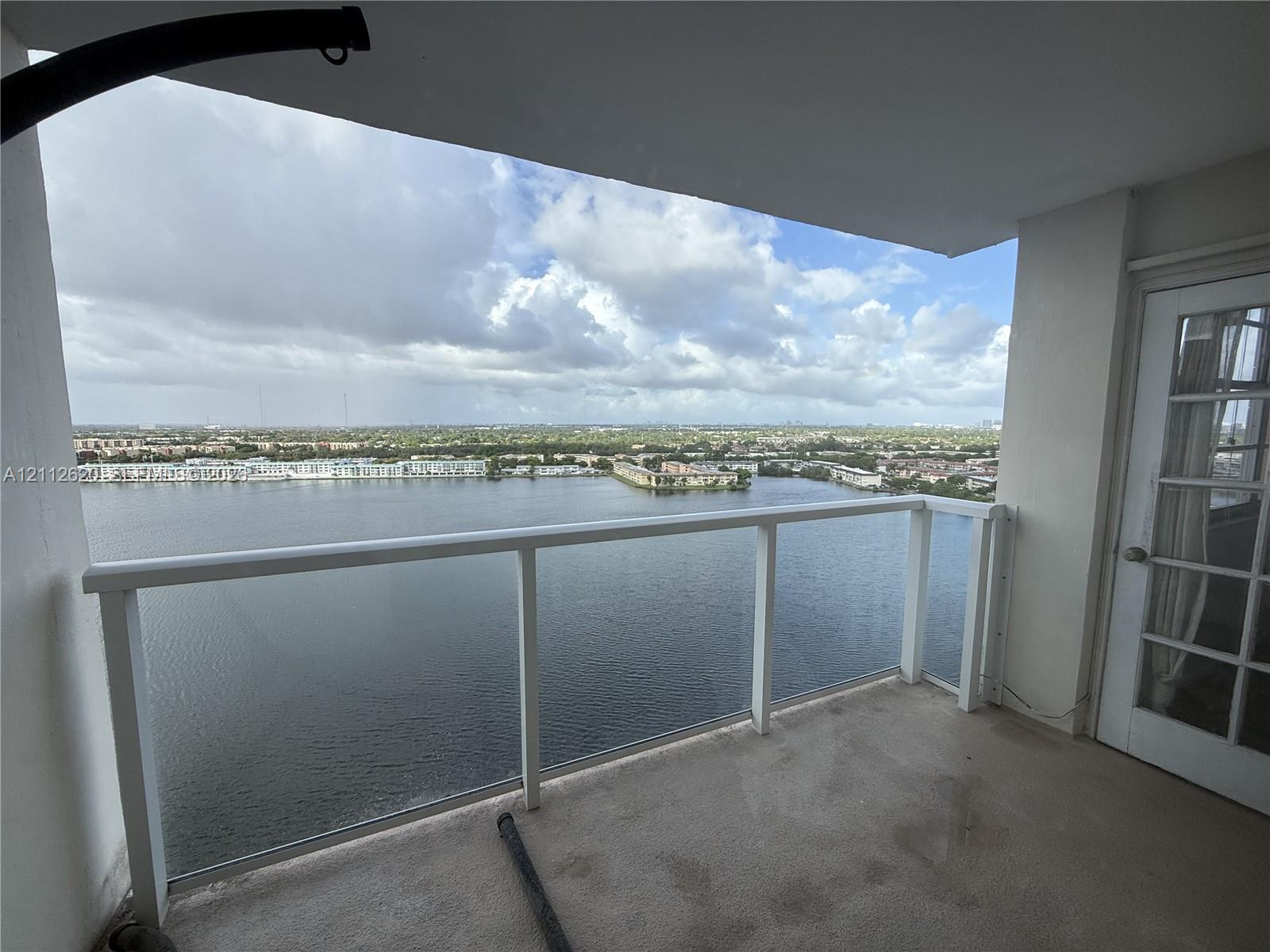 Covered balcony featuring a white railing and a door with glass panes, overlooking an expansive water expanse and horizon
