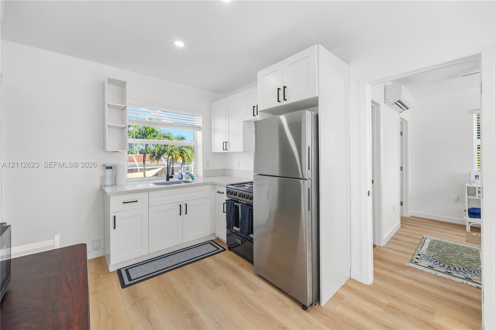 Kitchen featuring white cabinetry with black hardware, stainless steel refrigerator, dark range, light-toned wood-finish flooring, and quartz countertops