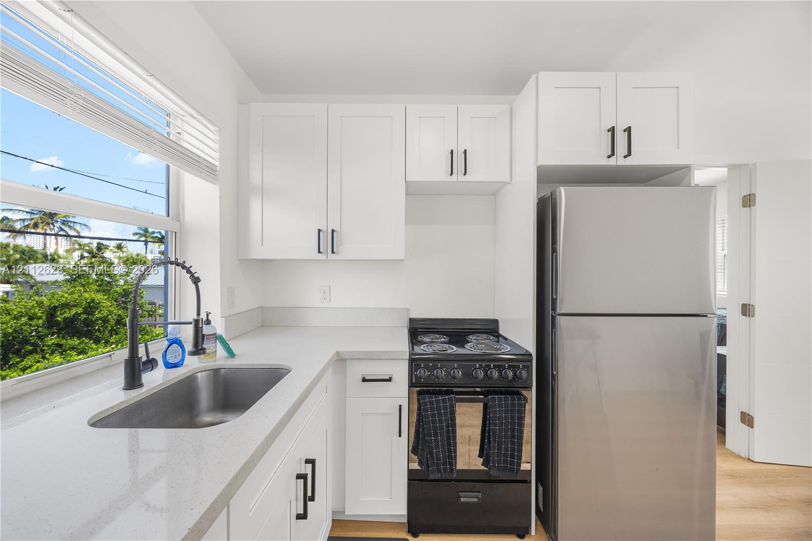Kitchen featuring white shaker-style cabinetry, matte black hardware, stone-finish countertops, stainless steel refrigerator, and high-arc pull-down faucet