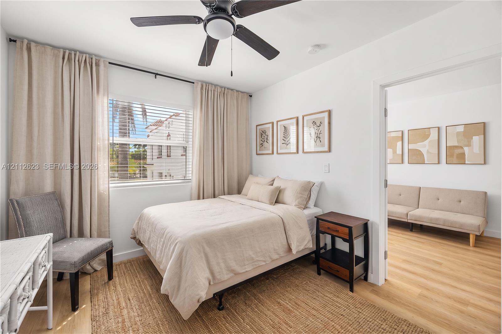 Neutral-toned interior featuring wood-finish flooring, a ceiling fan with integrated lighting, and a window with horizontal blinds