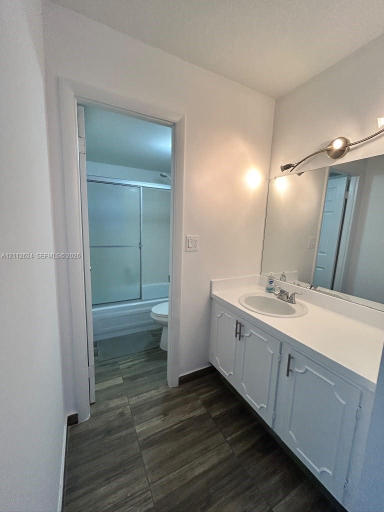 Bathroom featuring a white vanity with an integrated countertop, oval basin, expansive wall-mounted mirror, brushed-finish light fixture, and wood-finish tile flooring
