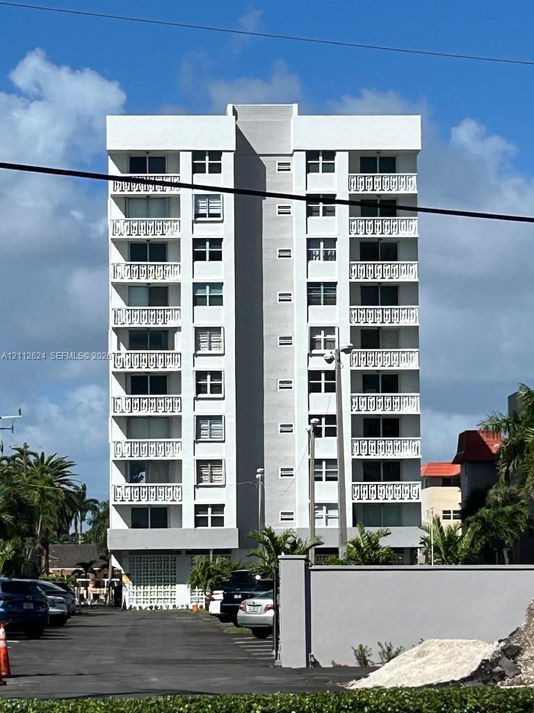 Multi-story residential building featuring a white facade, symmetrical balconies with decorative railings, and ground-level patterned concrete block screening