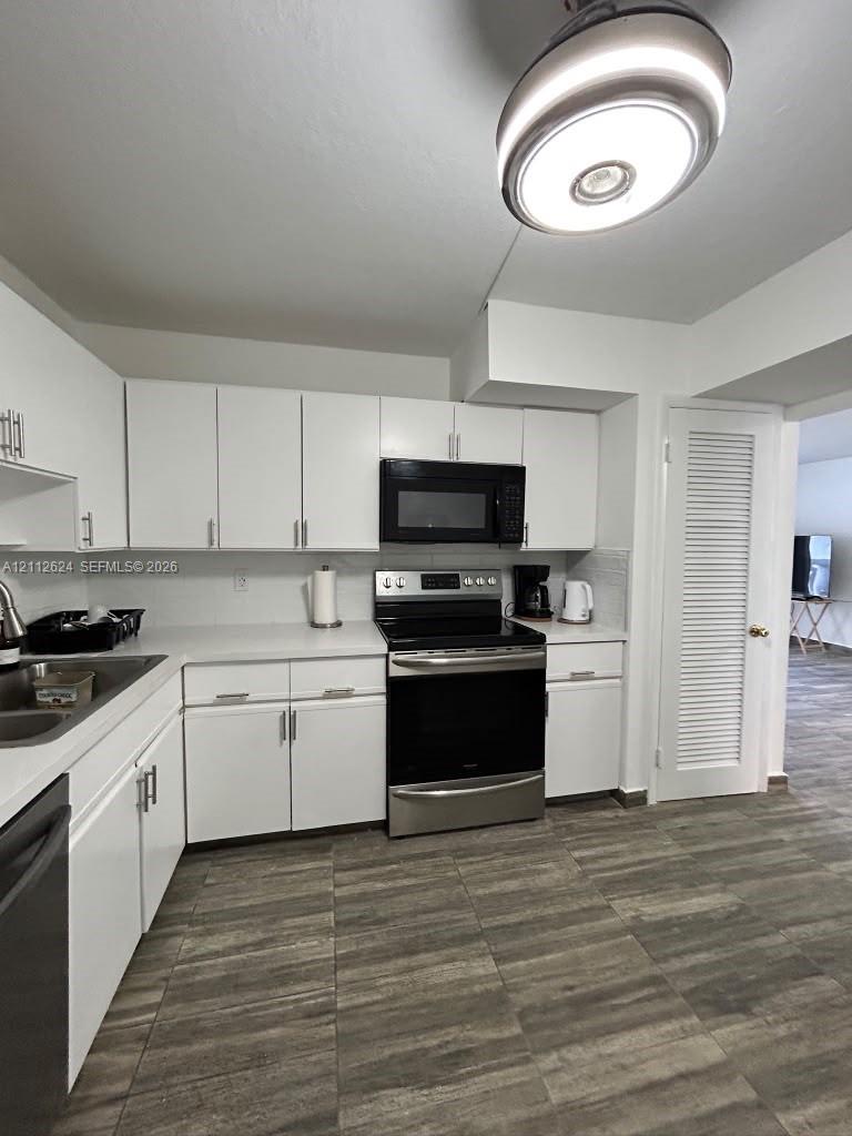 Kitchen featuring white cabinetry with brushed nickel hardware, stainless steel appliances, a modern flush-mount light fixture, and wood-finish tile flooring