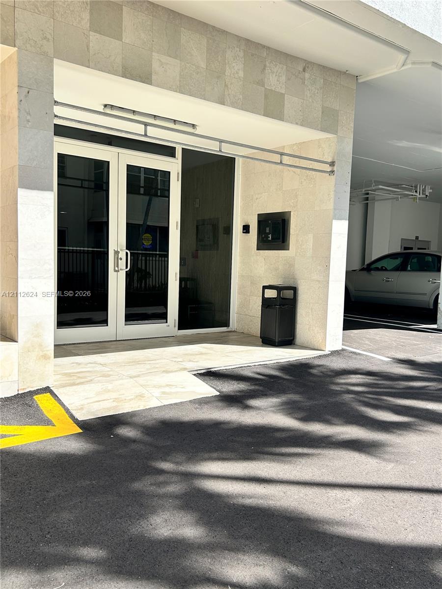 Building entrance featuring dual-panel glass doors, natural stone tile facade, and integrated electronic security access system