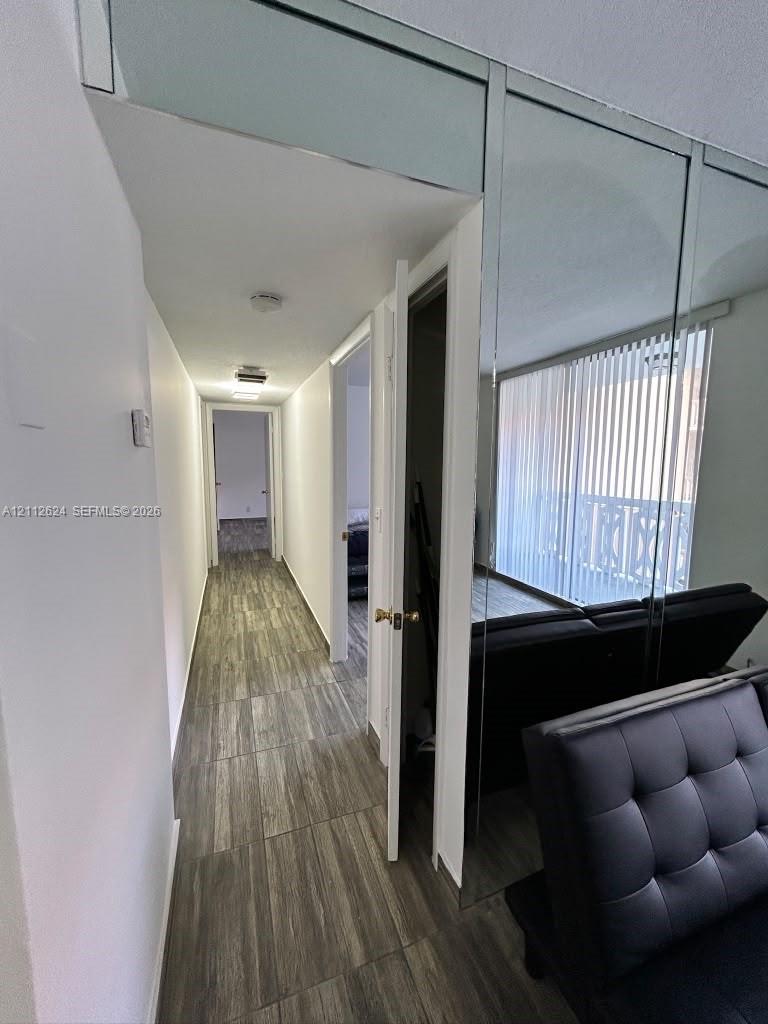 Hallway featuring wood-finish flooring, floor-to-ceiling mirrored wall paneling, and vertical blinds