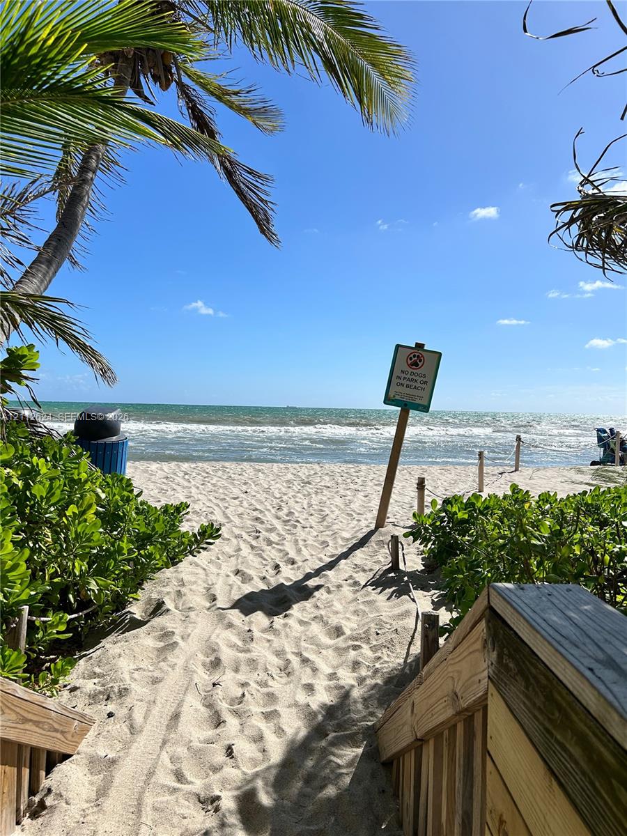 Sandy beach access featuring wooden stairs with handrails, mature palm trees, and coastal vegetation