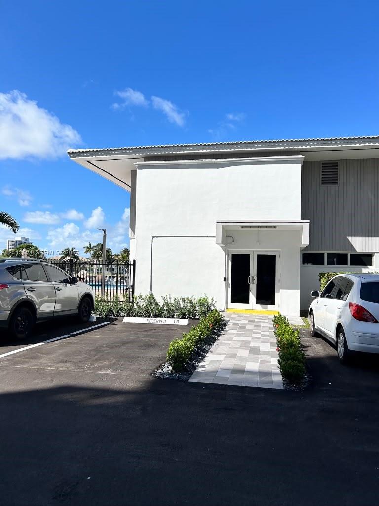 Exterior entrance featuring double glass doors, a stone-tiled walkway, and manicured landscaping