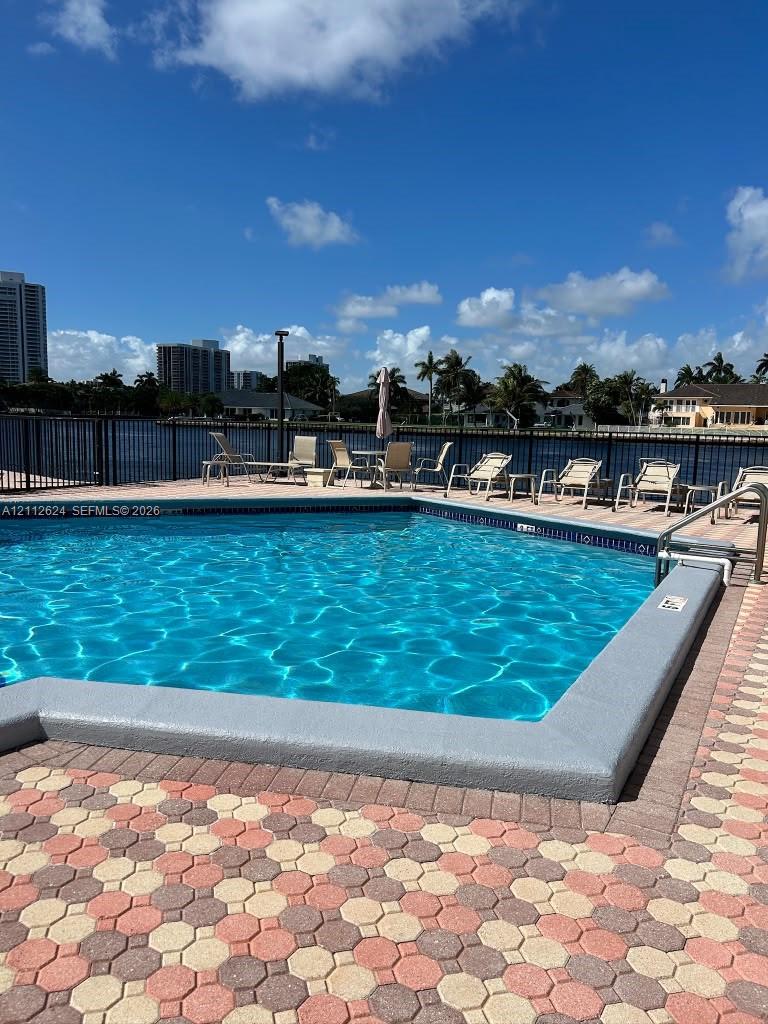 In-ground pool with concrete coping, decorative paver decking, and a metal perimeter fence overlooking the waterway