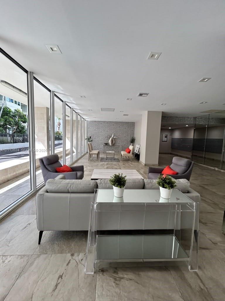 Floor-to-ceiling glass windows, recessed ceiling lighting, large-format tiled flooring, and a textured stone-finish accent wall