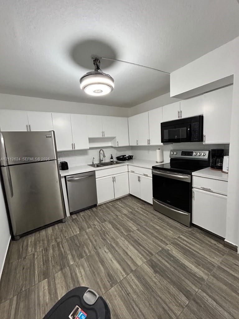 Kitchen featuring white cabinetry, solid-surface countertops, stainless steel appliances, and wood-finish flooring