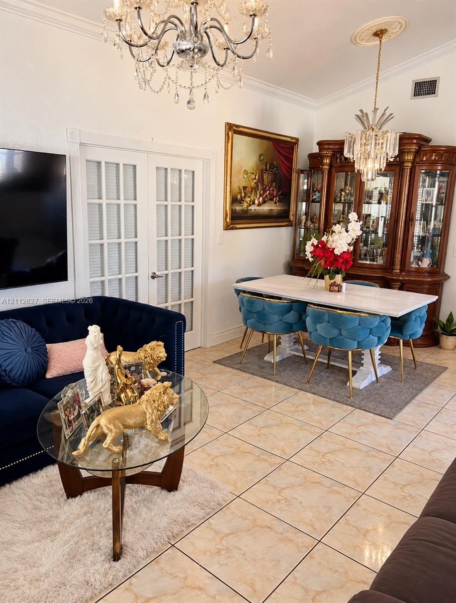 Interior space featuring large-format tile flooring, crown molding, double French doors, and decorative crystal chandeliers with ceiling medallions