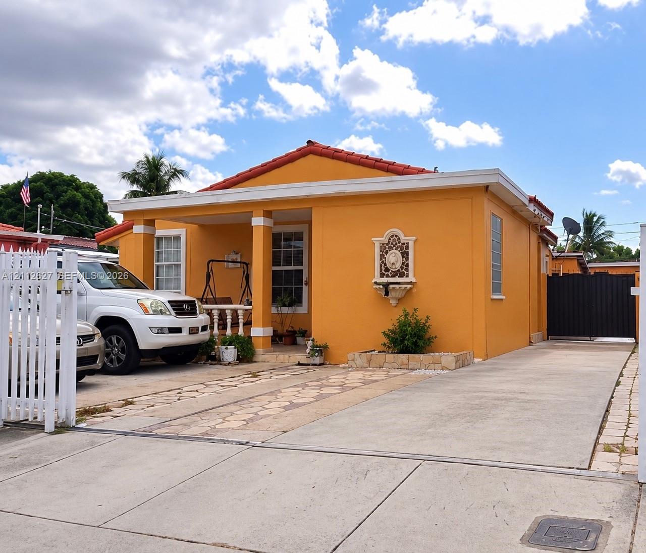 Single-story home featuring a tile roof, covered front porch with square columns, decorative wall-mounted exterior fountain, and a paved driveway with a privacy gate