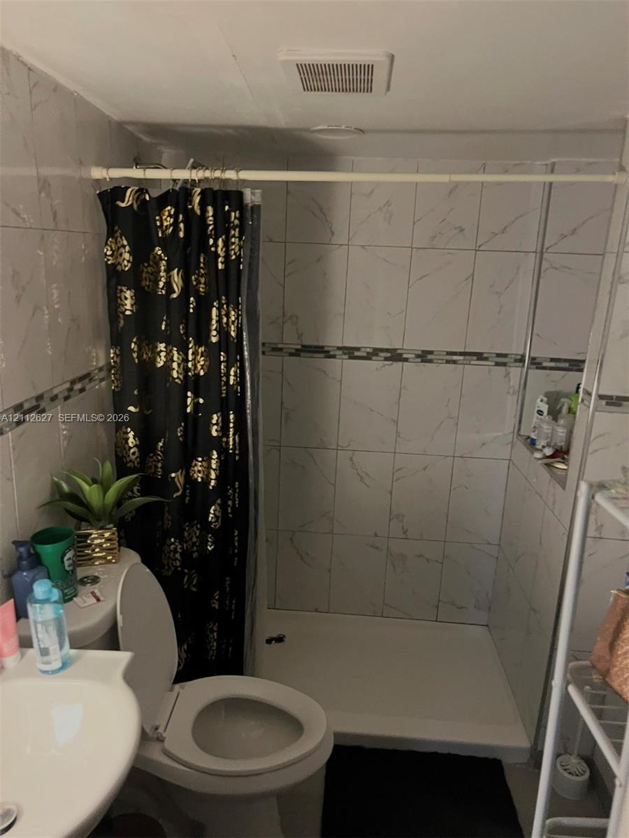 Bathroom featuring a walk-in shower with white veined tile surround, decorative mosaic tile accents, and a built-in recessed shelf