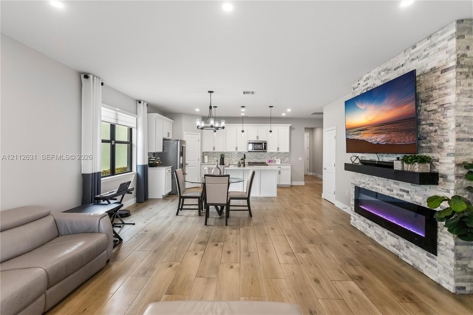 Open-concept interior featuring wood-finish flooring, a full-height stone-clad fireplace with an integrated linear electric insert, white cabinetry, and recessed lighting