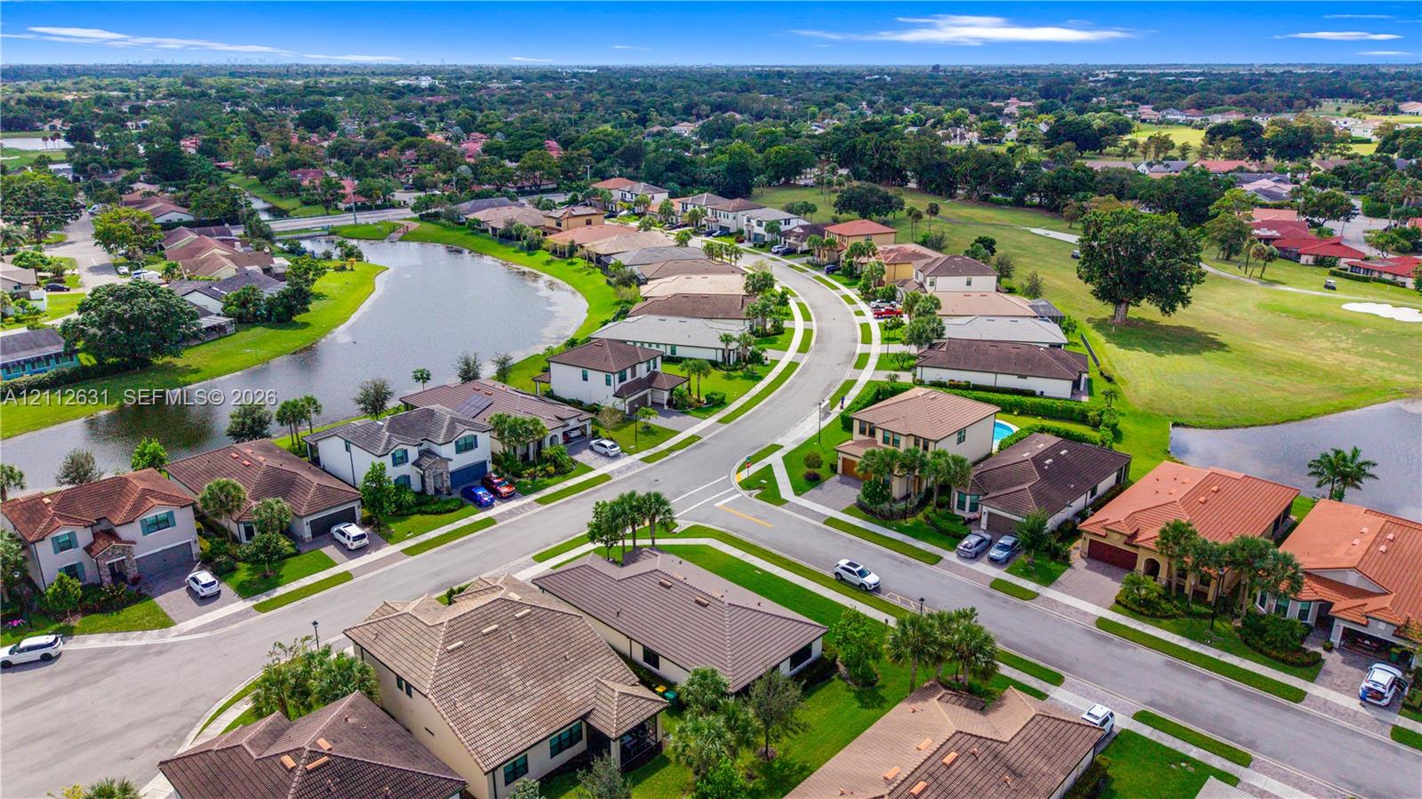 Aerial perspective of residential neighborhood featuring a winding lake, paved streets, manicured green space, and tile-roofed homes