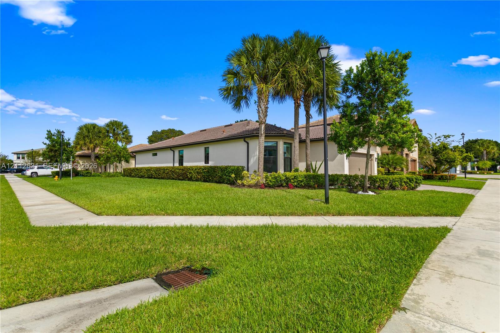 Corner lot featuring a stucco exterior, a tiled roof, mature palm trees, and manicured hedges Corner lot featuring a stucco exterior, a tiled roof, mature palm trees, and manicured hedges