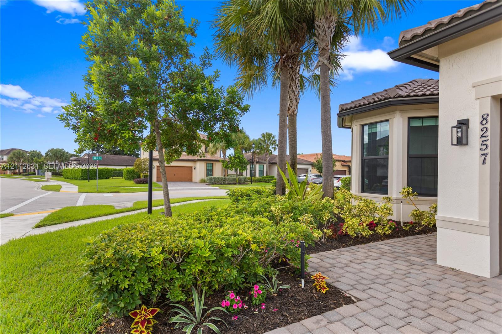 Stucco exterior featuring a tiled roof, paved entryway, and manicured landscaping with established palm trees