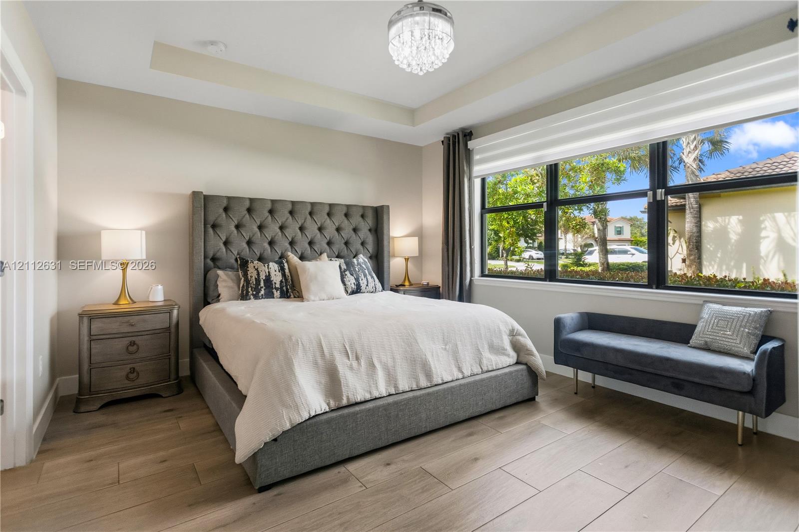 Bedroom featuring wood-finish flooring, a tray ceiling, a multi-tiered crystal chandelier, and large windows with black frames