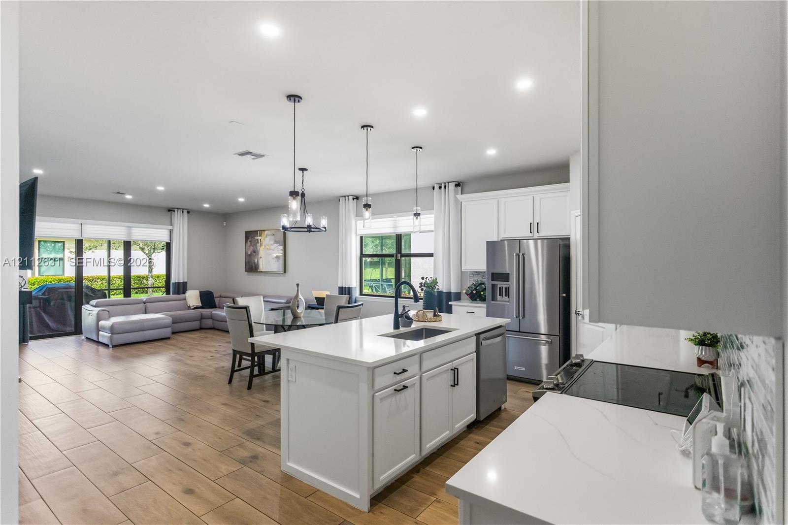 Kitchen featuring white shaker-style cabinetry, quartz countertops, stainless steel appliances, an island with an undermount sink, and wood-finish tile flooring