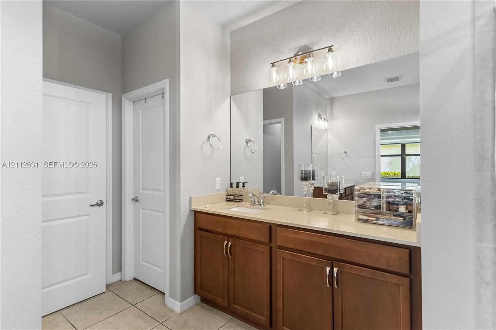 Bathroom vanity featuring a light-toned countertop, rectangular undermount sink, warm wood-finish cabinetry, a large wall-to-wall mirror, and multi-bulb integrated lighting