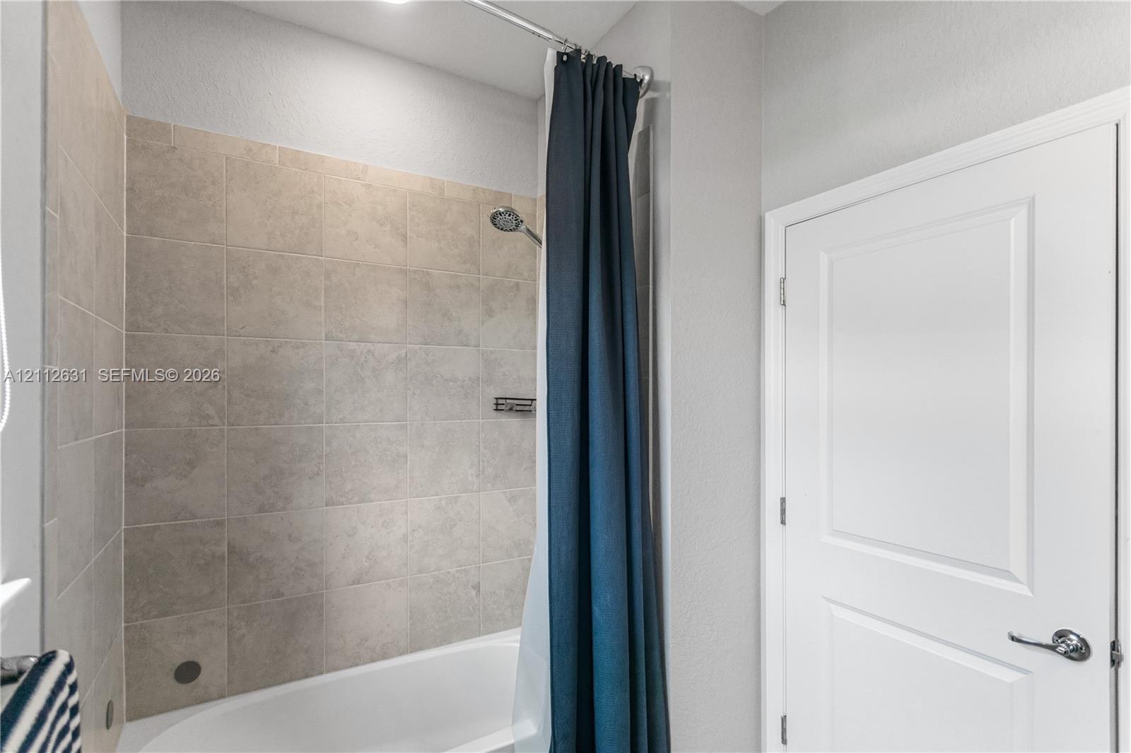Bathtub with a shower head, tiled surround, built-in shelving niche, and a panel door with brushed metal hardware