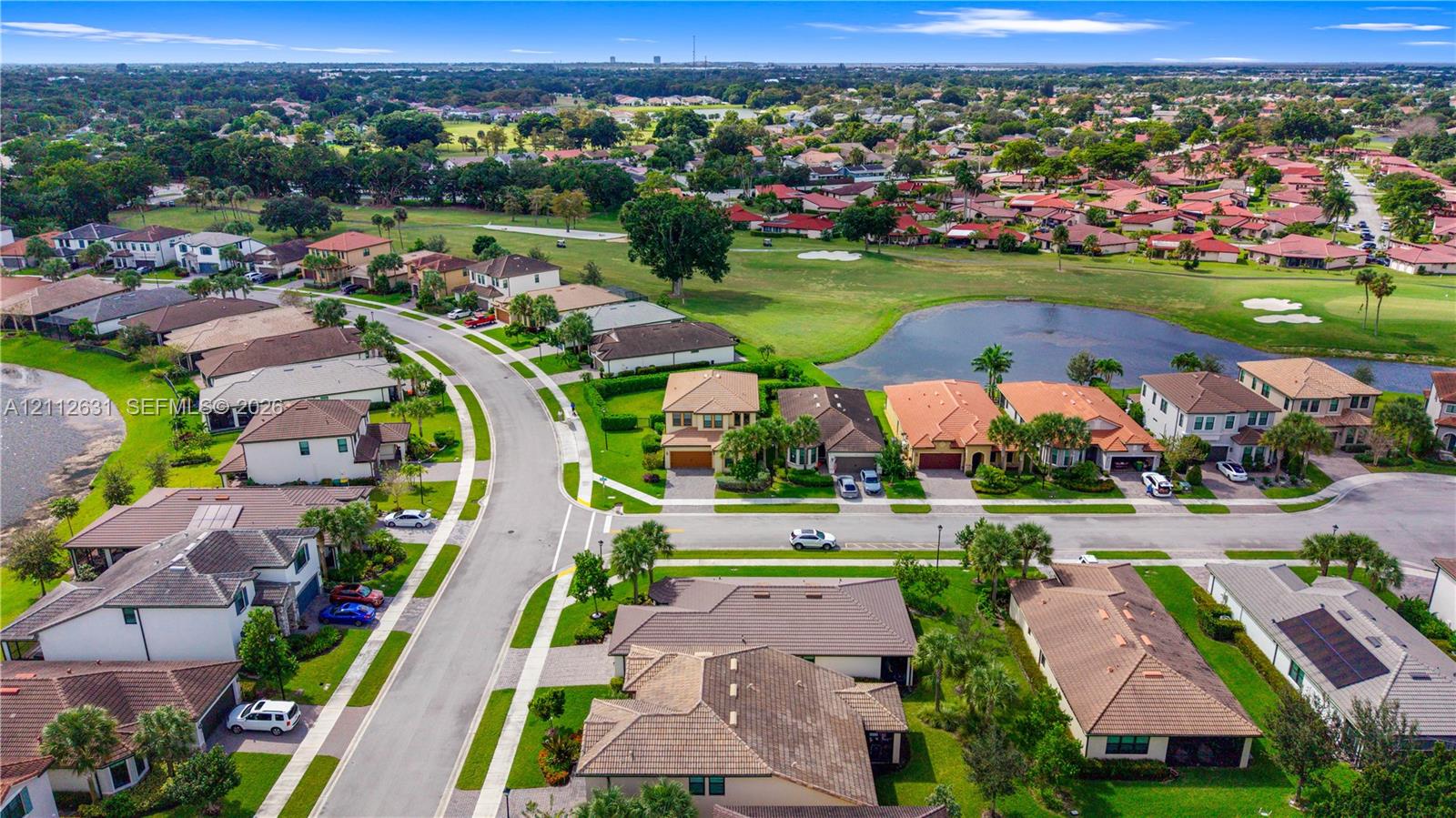 Aerial perspective featuring multi-story residential structures, paved street infrastructure, landscaped green spaces, and a neighborhood water feature