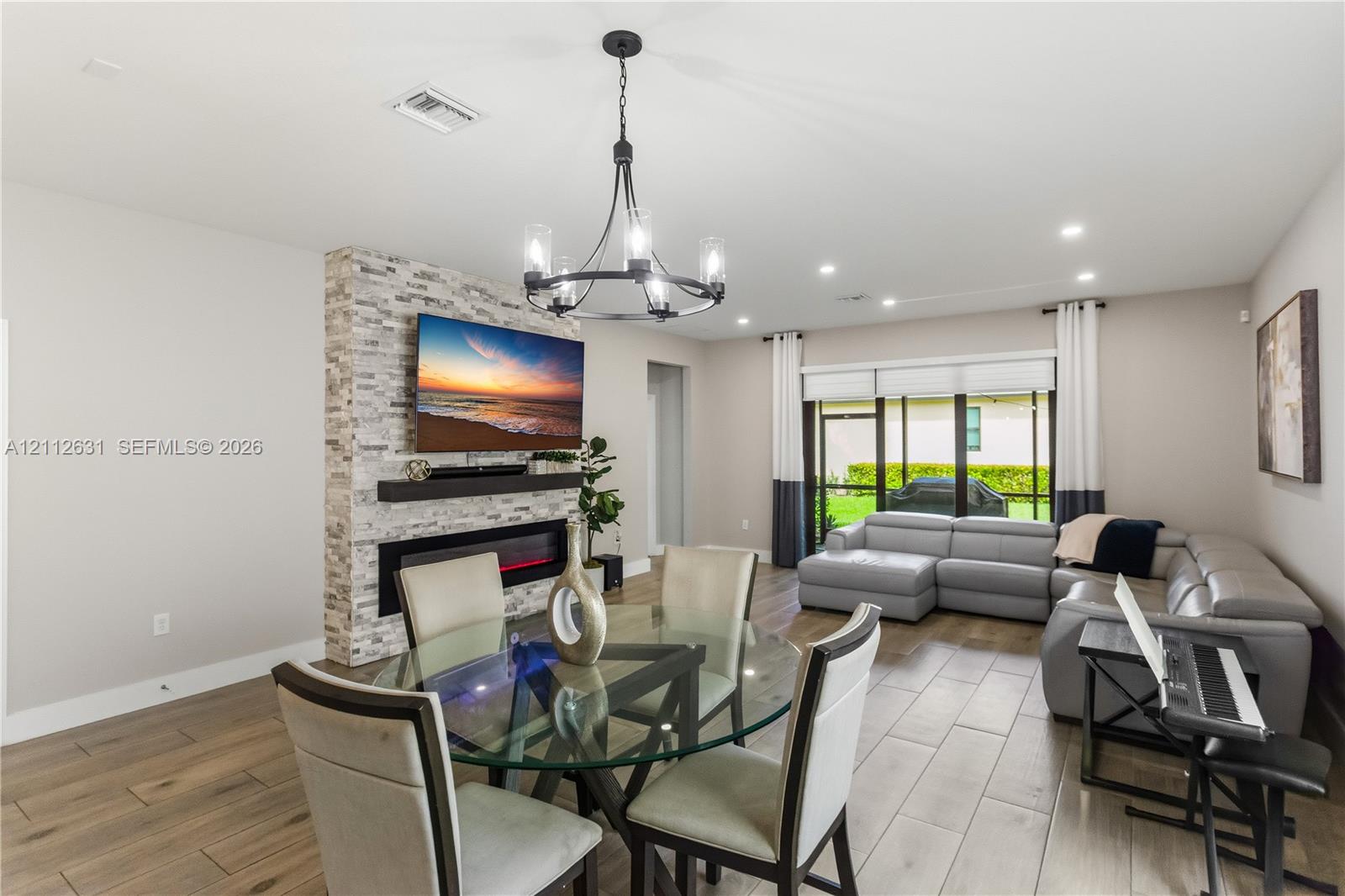 Open-concept area featuring wood-finish flooring, a floor-to-ceiling stone-cladding fireplace surround, a built-in linear electric fireplace, and a decorative metal chandelier