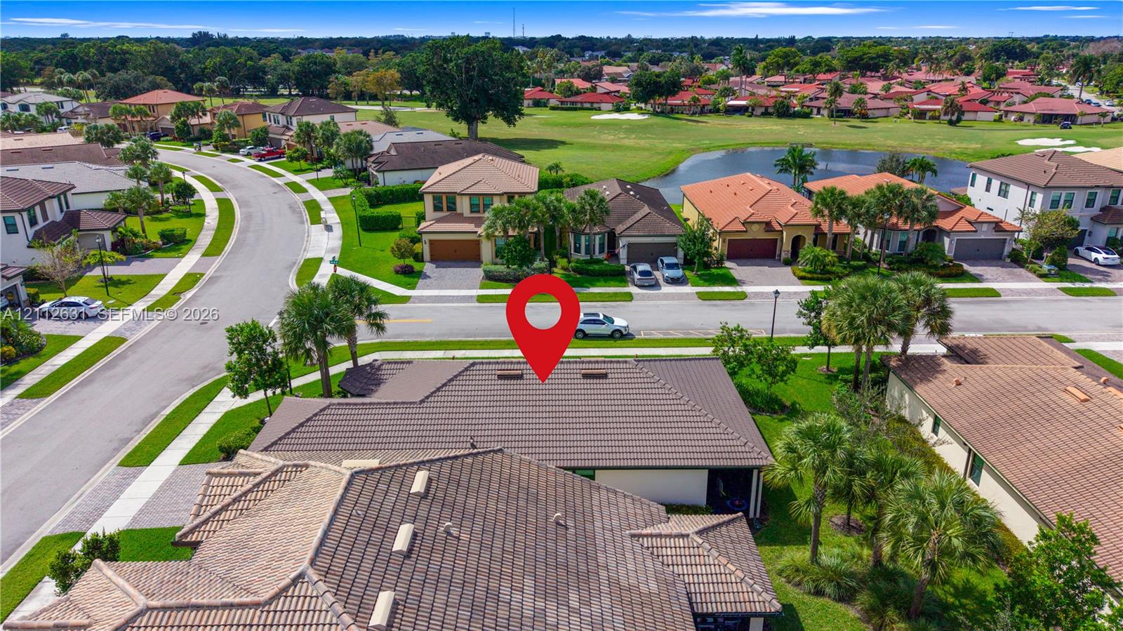 Aerial perspective featuring a multi-gabled tiled roof structure with integrated skylights, positioned within a landscaped residential community featuring expansive manicured lawns and mature palm trees