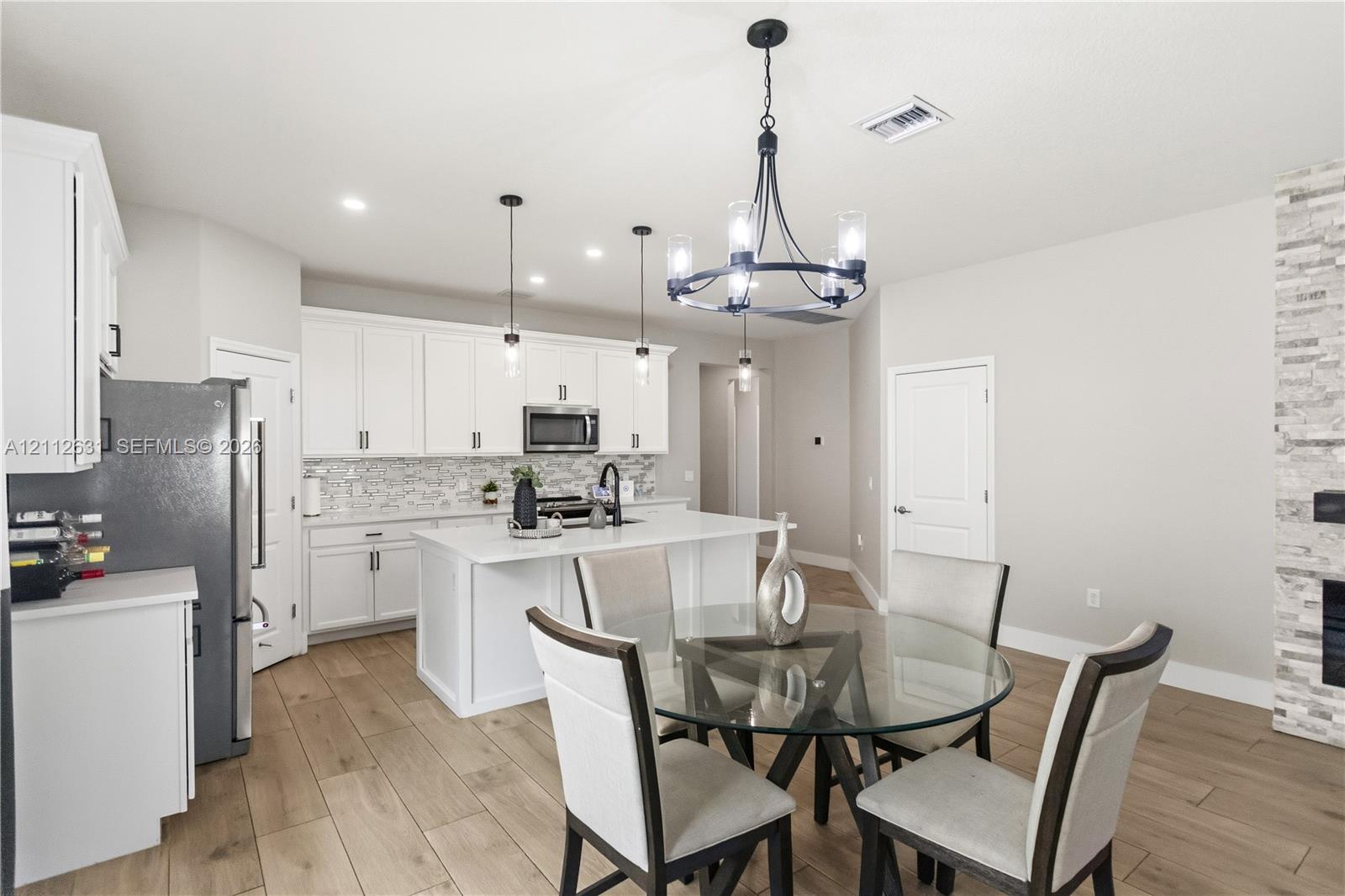 Kitchen featuring white cabinetry, quartz countertops, a central island, wood-finish flooring, and a stone-clad fireplace