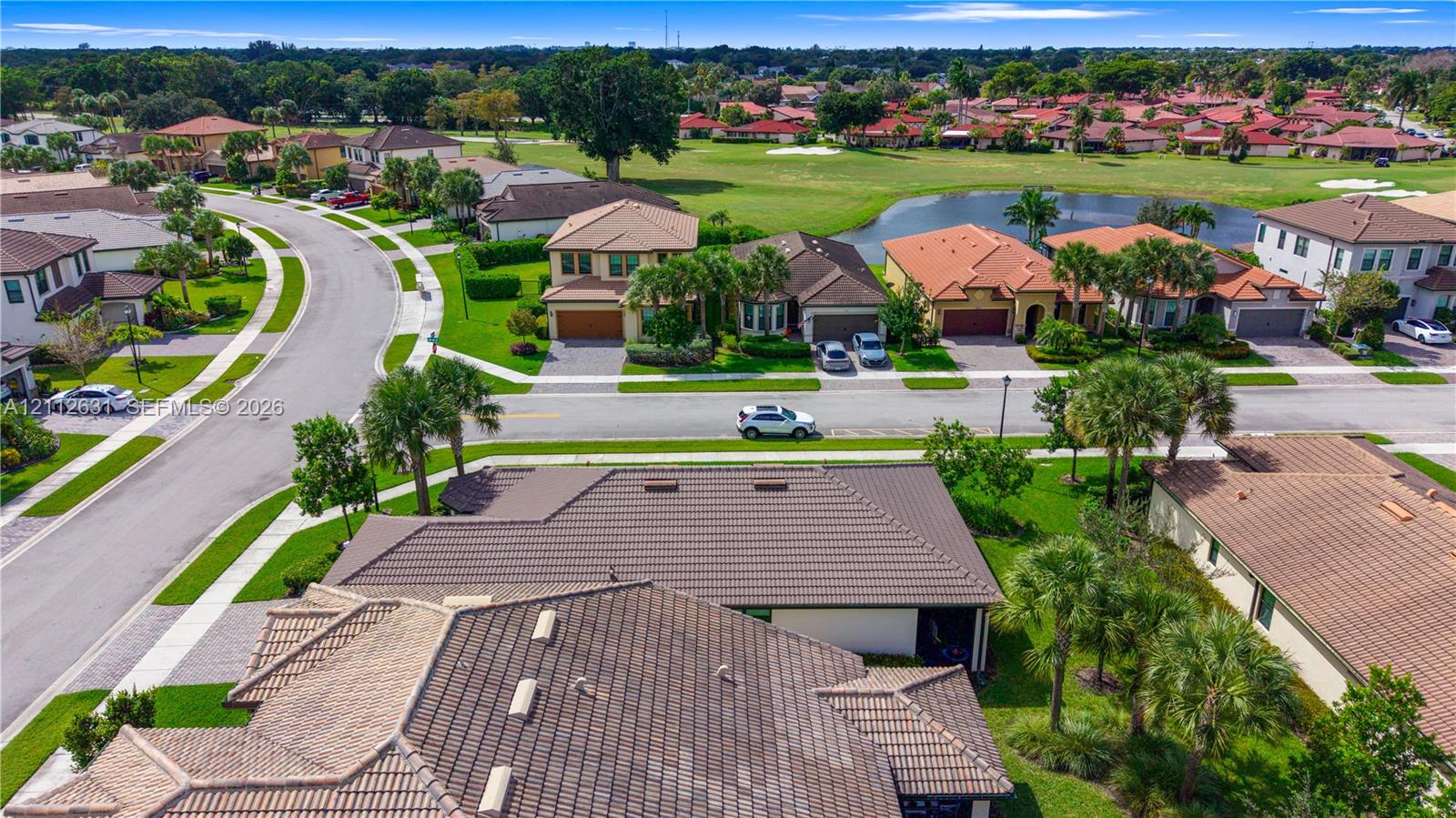 Aerial perspective of residential neighborhood featuring tile roofing, paved streets, manicured landscaping, and pond