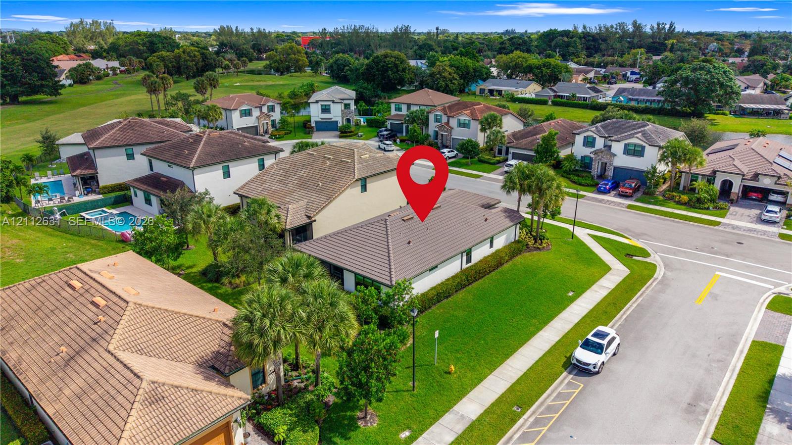 Aerial perspective of a corner lot property featuring a tiled roof, manicured lawn, and mature palm landscaping