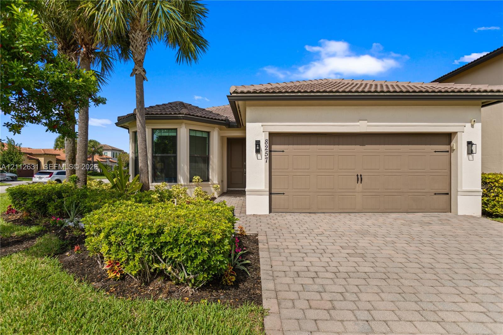 Stucco exterior featuring a tiled hip roof, multi-pane bay window, paved driveway, and established landscaping Stucco exterior featuring a tiled hip roof, multi-pane bay window, paved driveway, and established landscaping