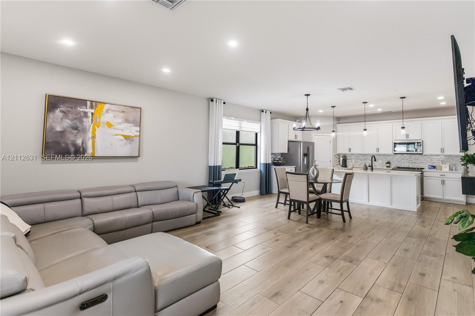 Open-concept living space featuring wood-finish flooring, recessed lighting, white shaker-style cabinetry, a kitchen island, and a decorative chandelier