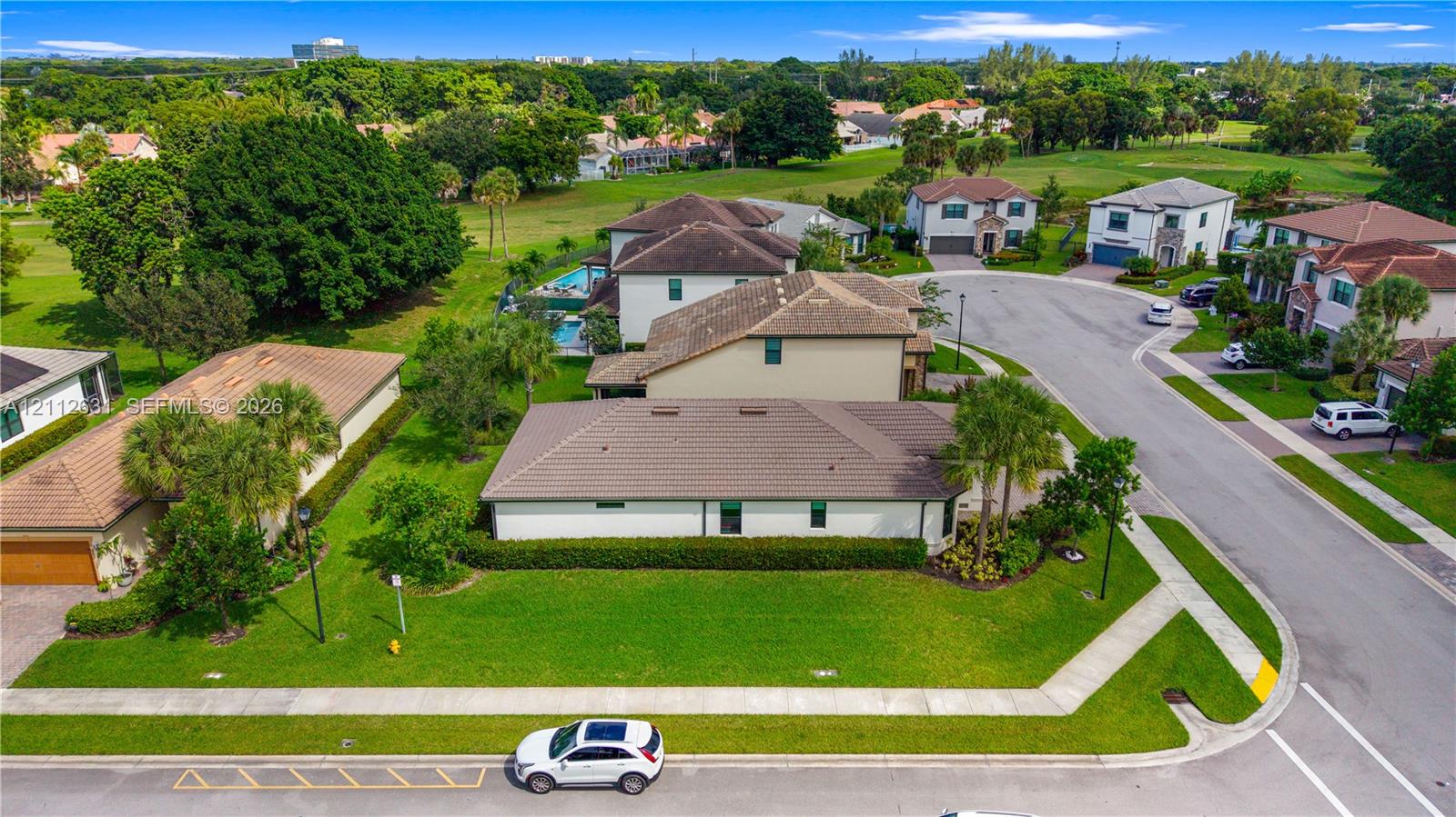Corner lot residence featuring a tile roof, multi-car garage, manicured landscaping, and expansive green space