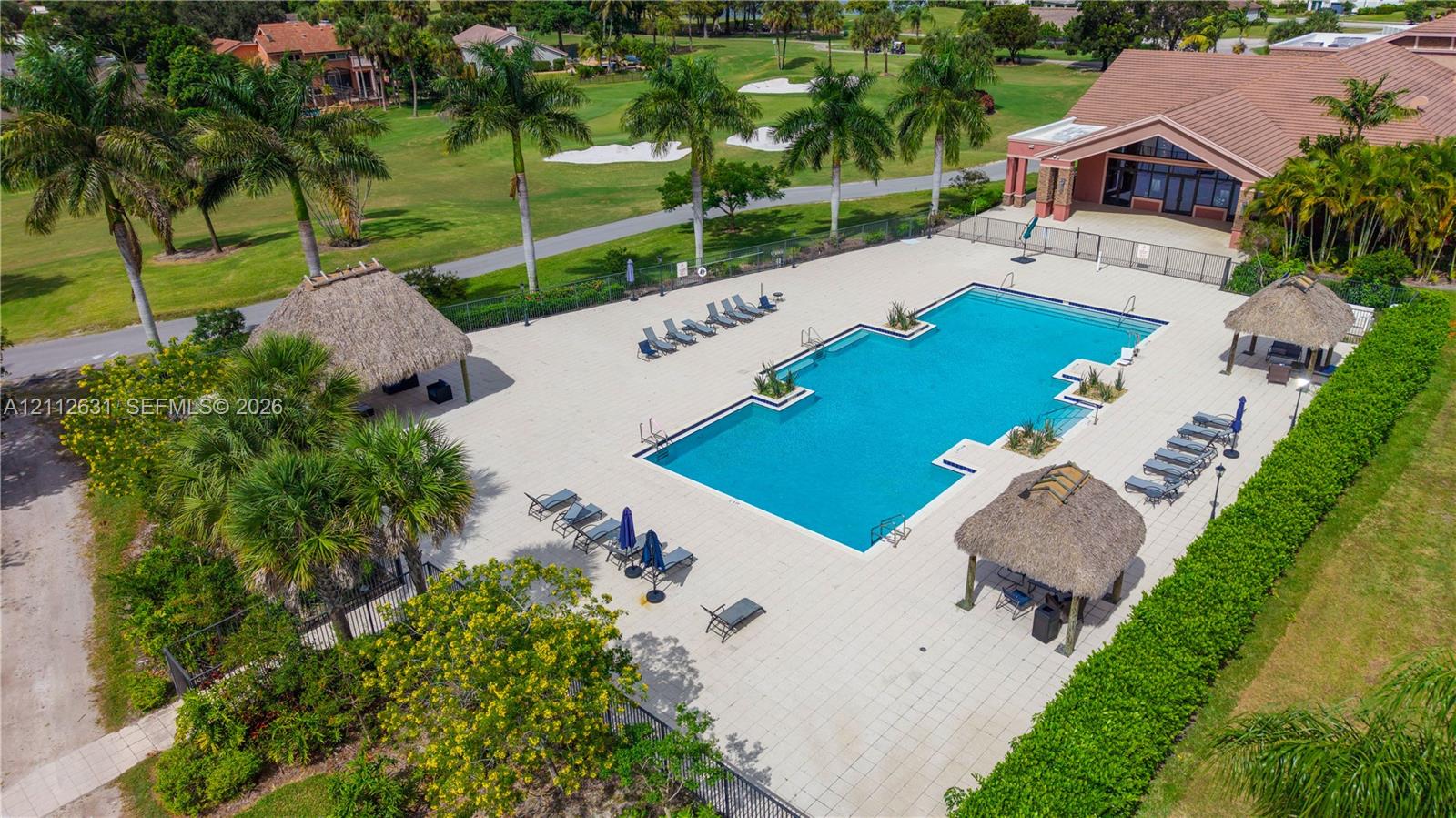 Rectangular swimming pool featuring a tiled deck, multiple thatched-roof structures, and perimeter landscaping