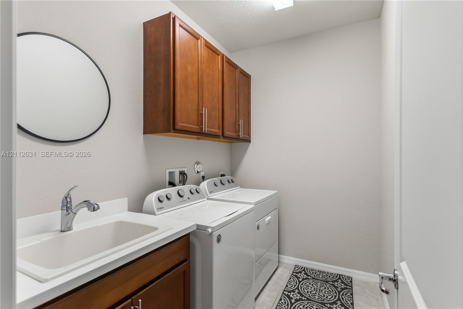 Laundry room featuring wood-finish cabinetry, a utility sink with a chrome faucet, and solid-surface countertop