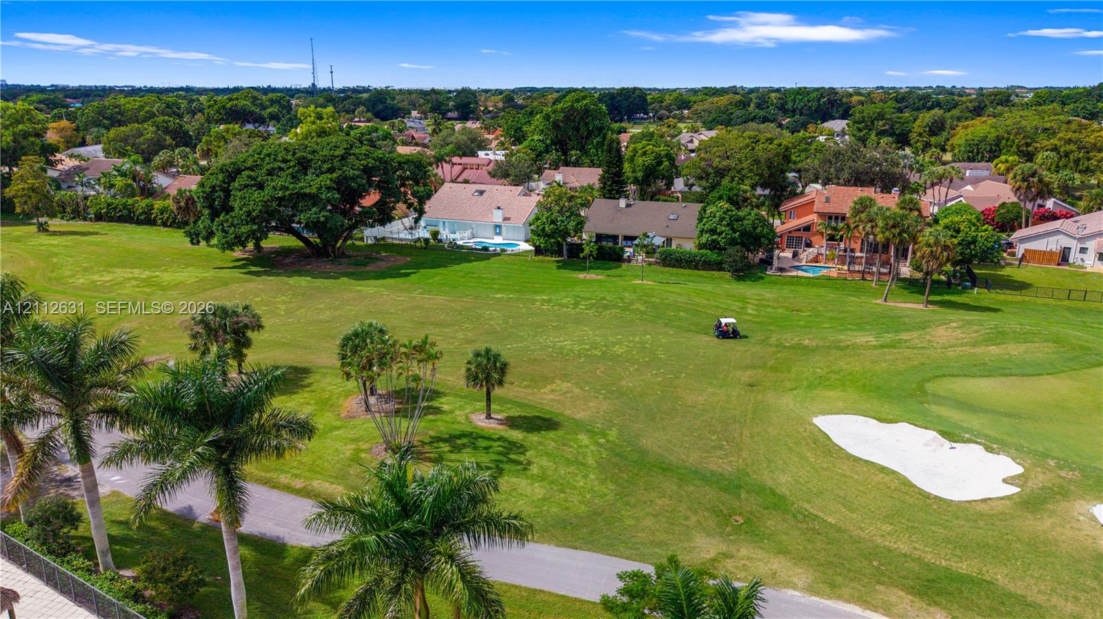 Aerial perspective of a golf course setting featuring expansive green fairways, sand bunkers, mature trees, and landscaped palms