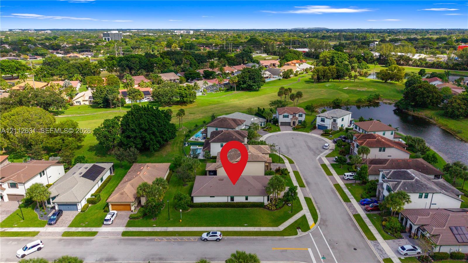 Aerial perspective of a corner-lot property featuring a multi-pitched shingled roof, manicured lawn, and paved driveway