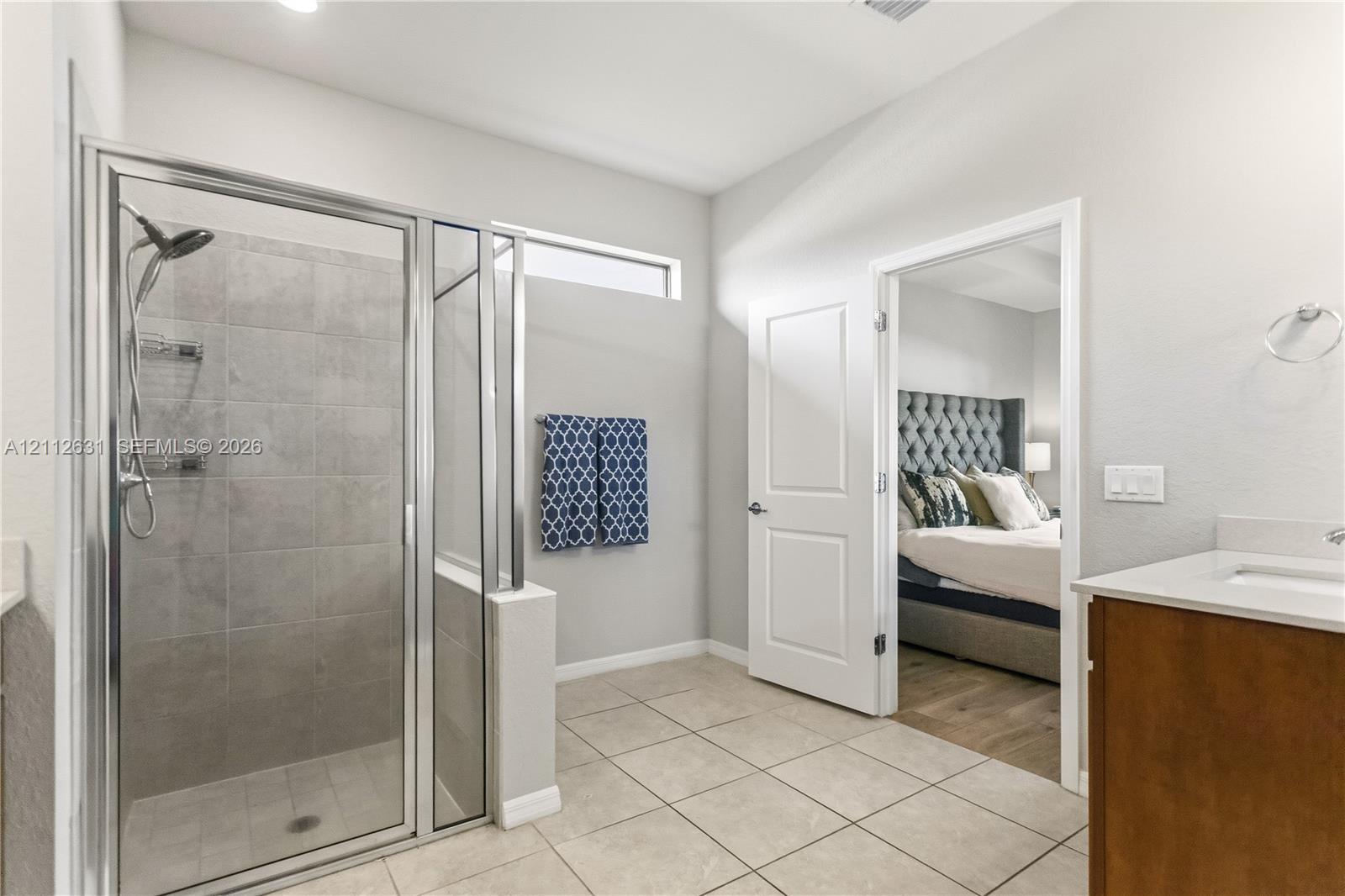 Walk-in shower with floor-to-ceiling ceramic tile surround and chrome fixtures, wood-finish vanity with countertop sink, and neutral ceramic tile flooring
