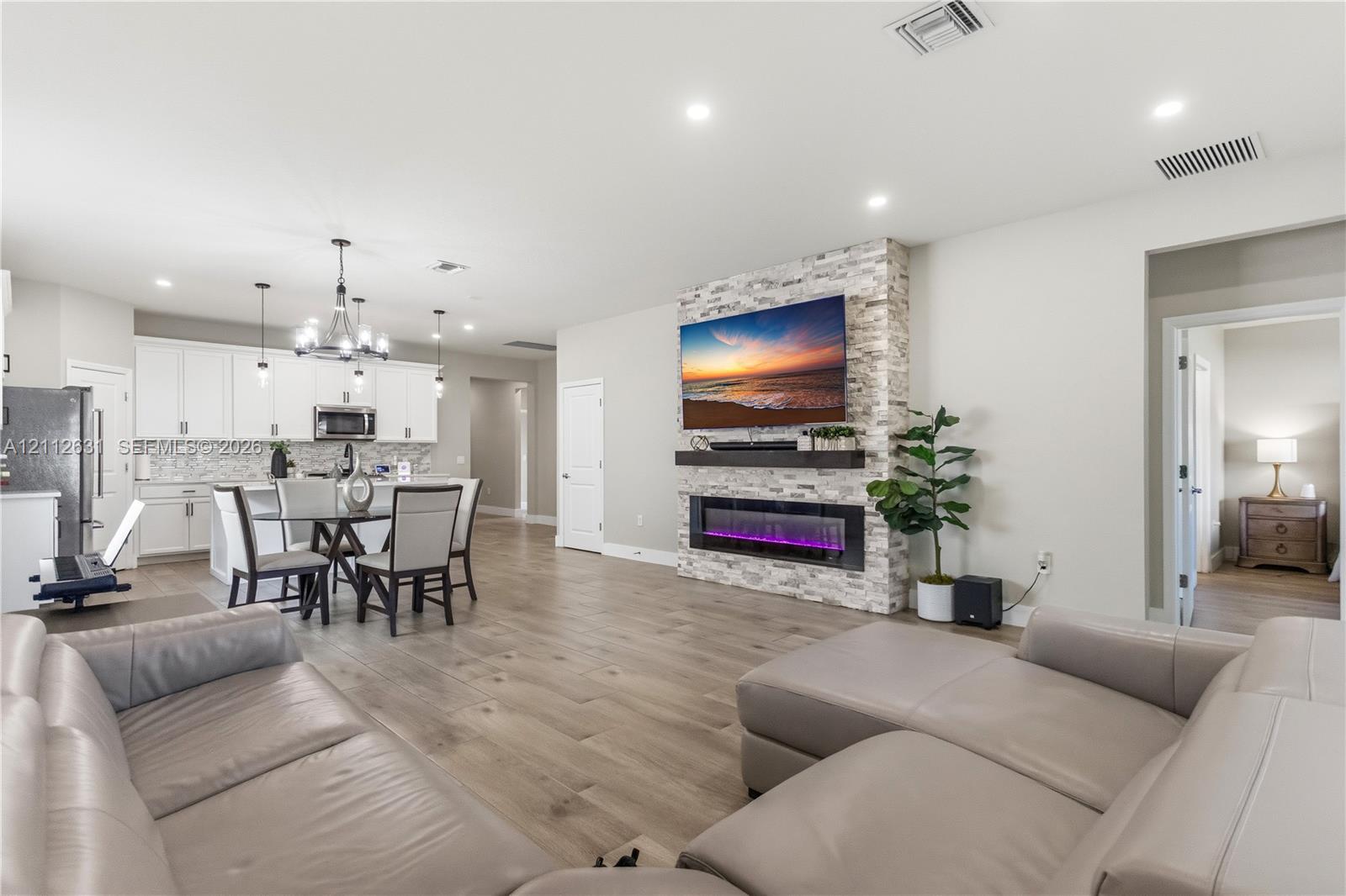 Open-concept living space featuring wood-finish flooring, recessed lighting, and a floor-to-ceiling stone-veneer fireplace with an integrated electric insert and floating mantel