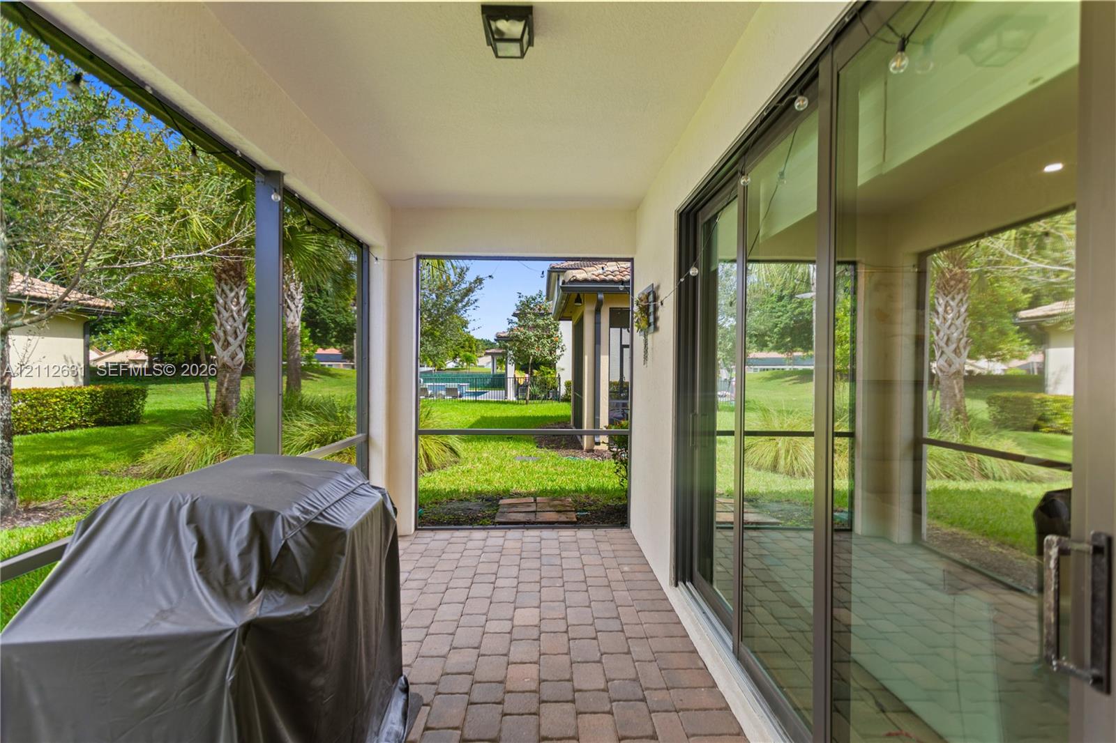 Screened-in lanai featuring paver flooring, overhead lighting, and multi-panel sliding glass doors